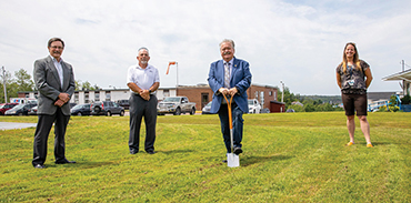 Four men and 1 woman social distanced breaking ground on new hospital with old hospital in the background