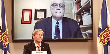 NS Premier Tim Houston hosting a press conference with Dr. Rob Strang attending virtually and shown on large screen in background