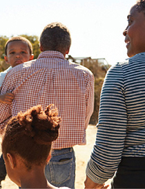 Family of four walking with back toward camera; mother holding young girl's hand and father carrying toddler boy)