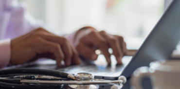 hands typing on a laptop computer with stethoscope nearby