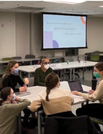 5 mask-wearing adult learners in dicussion at a desk