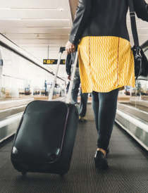 a femaile traveller walking on a people mover while carrying a carry on suitcase behind her