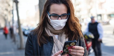 woman wearing a mask while outdoors and looking at her cellphone