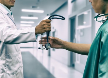 physician hands to another physician, a stethascope in a hallway